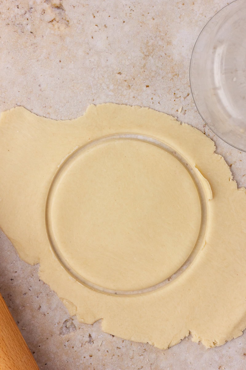 Pie dough is rolled thin on the counter while a glass cuts out a perfect five-inch circle.