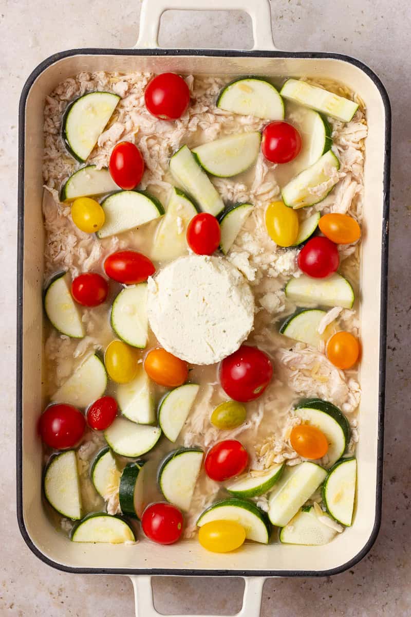 Unbaked Boursin chicken orzo casserole with zucchini, cherry tomatoes, and a round of Boursin cheese in the center.