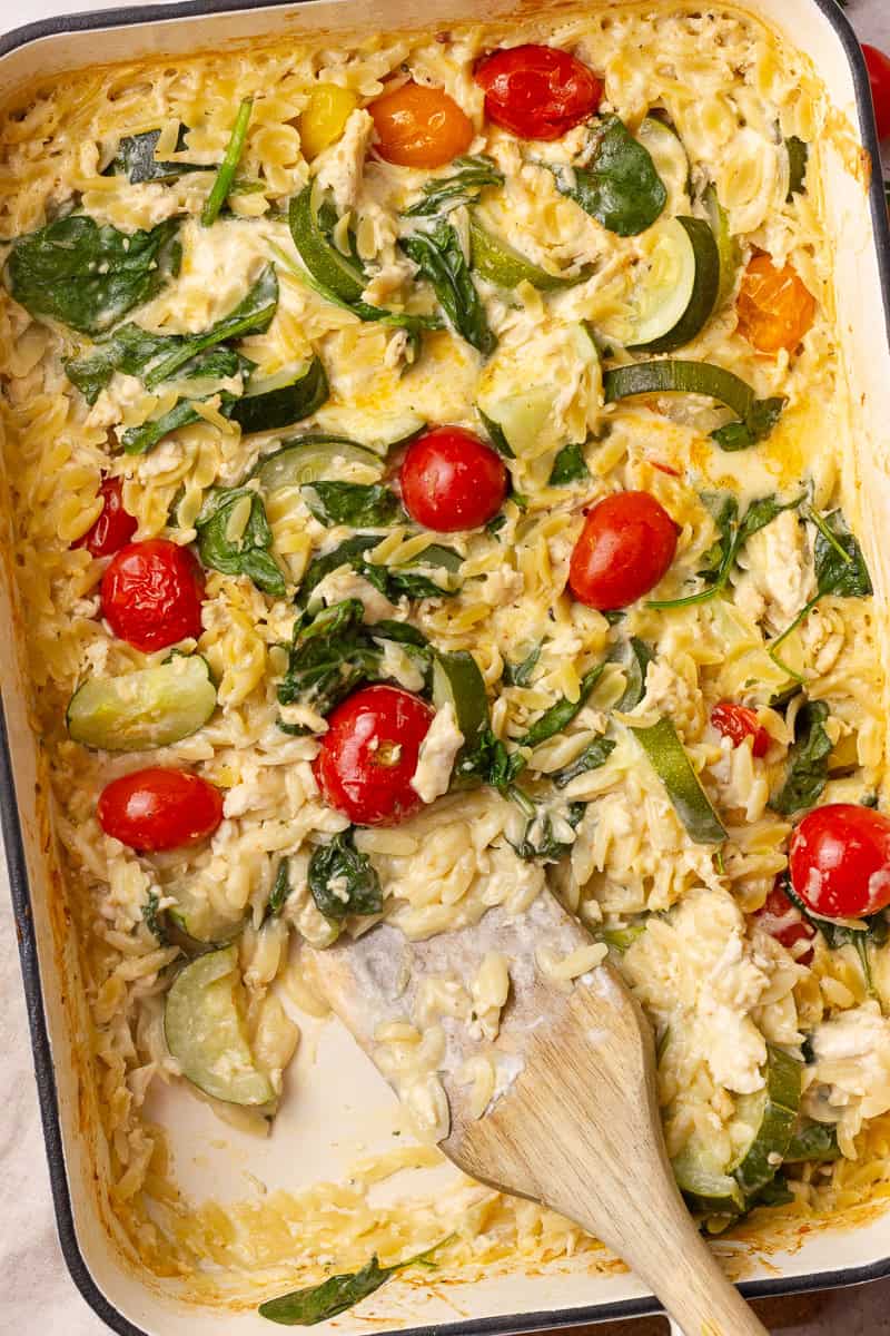 Close-up of the creamy chicken and orzo bake showing melty cheese, wilted spinach, and juicy tomatoes.

