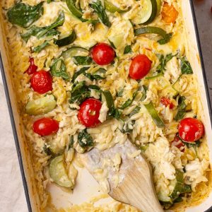 Overhead view of creamy baked Boursin chicken orzo with visible spinach, zucchini, and cherry tomatoes.