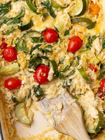 Overhead view of creamy baked Boursin chicken orzo with visible spinach, zucchini, and cherry tomatoes.