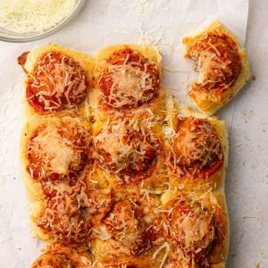A styled image with several sliders on white parchment paper with a bowl of shredded mozzarella cheese.
