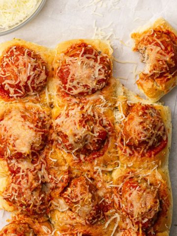 A styled image with several sliders on white parchment paper with a bowl of shredded mozzarella cheese.
