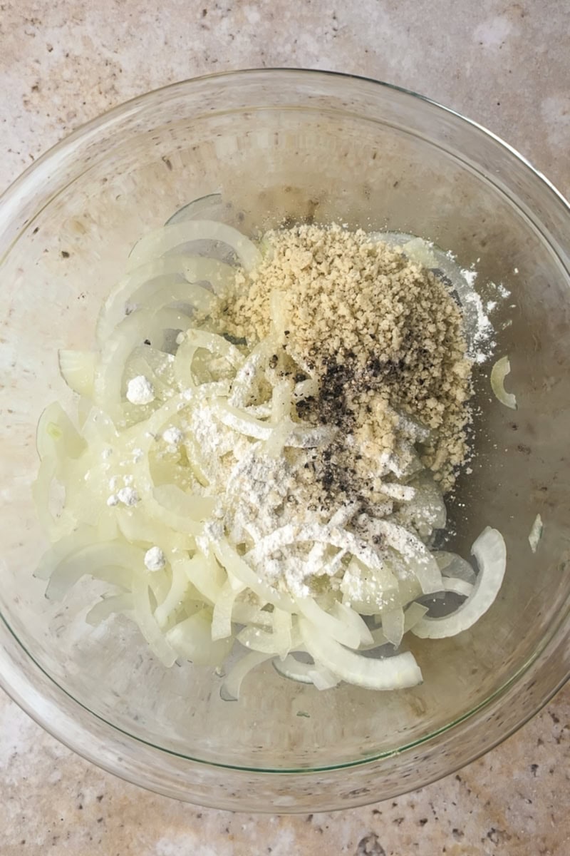 Thinly sliced onions tossed with flour and panko in a glass mixing bowl before baking.