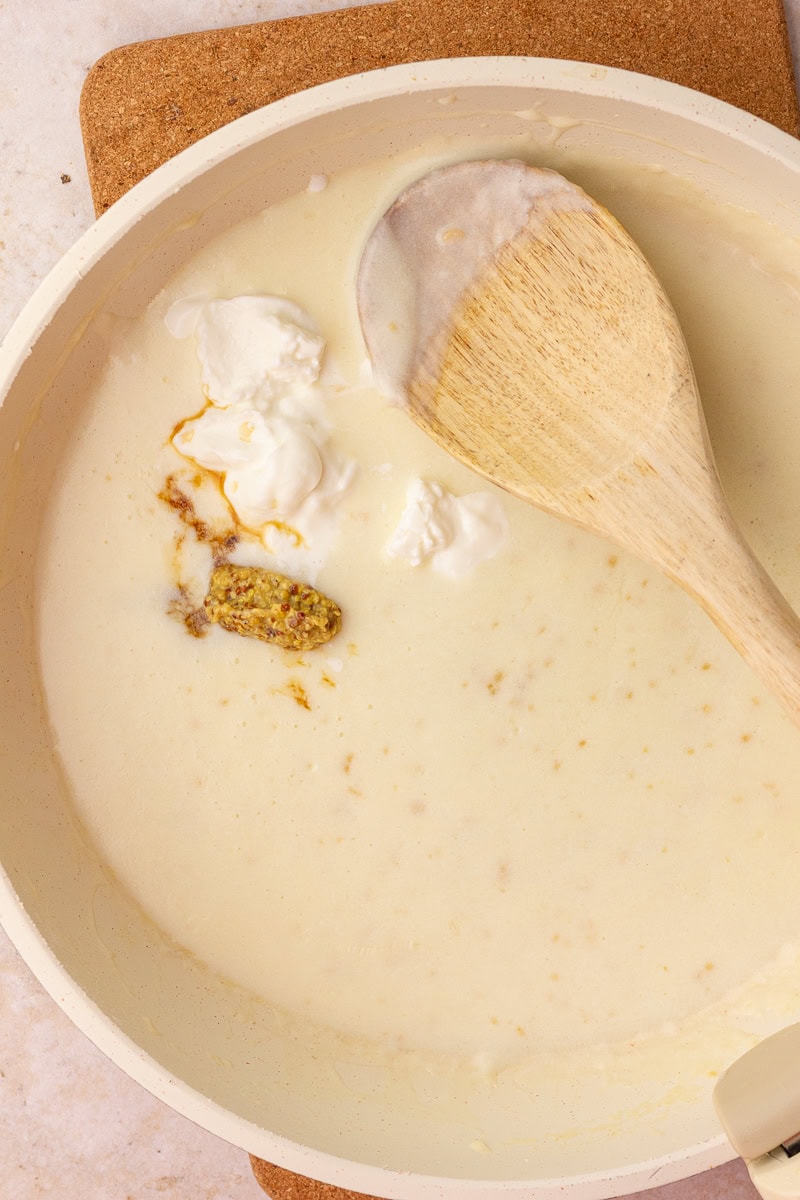 Whisking creamy sauce in a skillet with Greek yogurt, Dijon mustard, and seasonings just added.