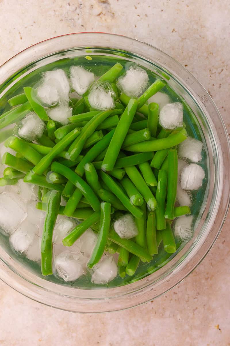 Fresh green beans cooling in a bowl of ice water after blanching.