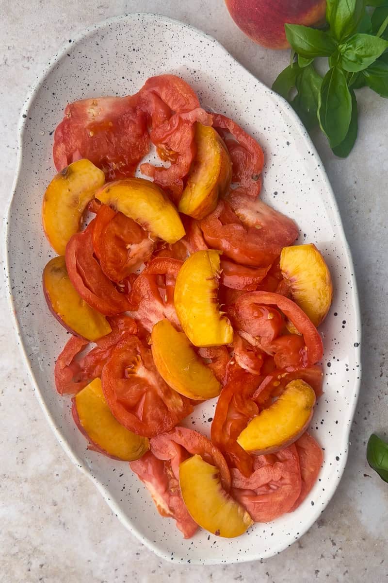 Sliced peaches and tomatoes arranged on a platter before adding burrata or toppings.
