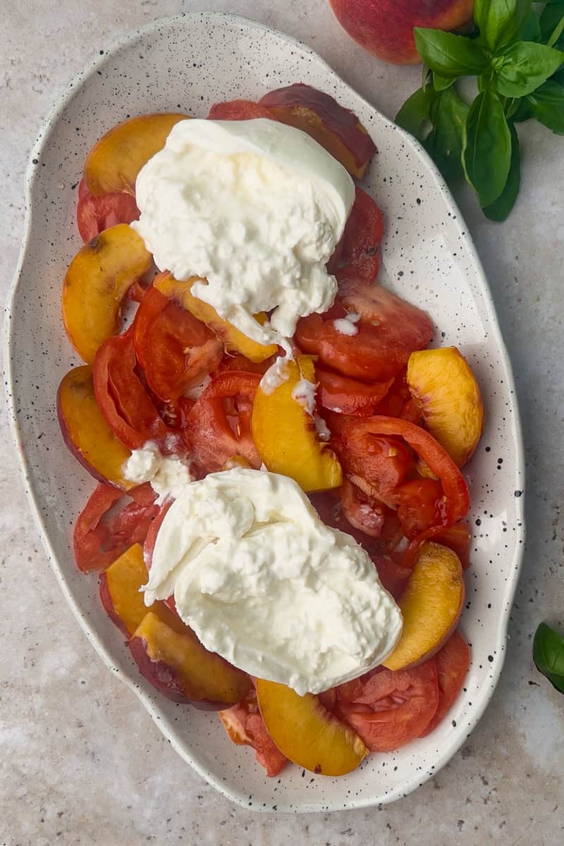 Burrata placed on top of the salad before any drizzle, highlighting the creamy cheese and colorful base.