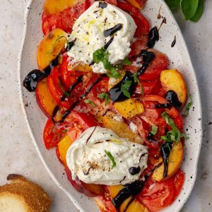 Styled hero shot of the finished peach tomato burrata salad with bread on the side and fresh basil garnish.