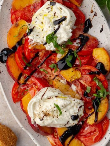Styled hero shot of the finished peach tomato burrata salad with bread on the side and fresh basil garnish.