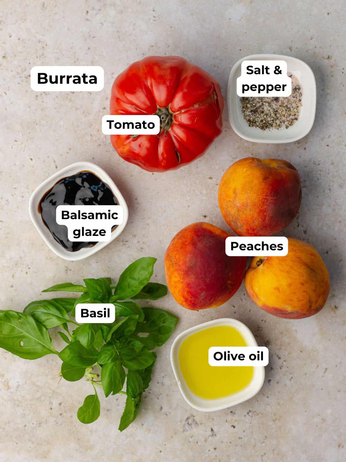 Flat lay of the main ingredients for the salad including burrata, peaches, tomato, basil, olive oil, balsamic glaze, and salt and pepper.