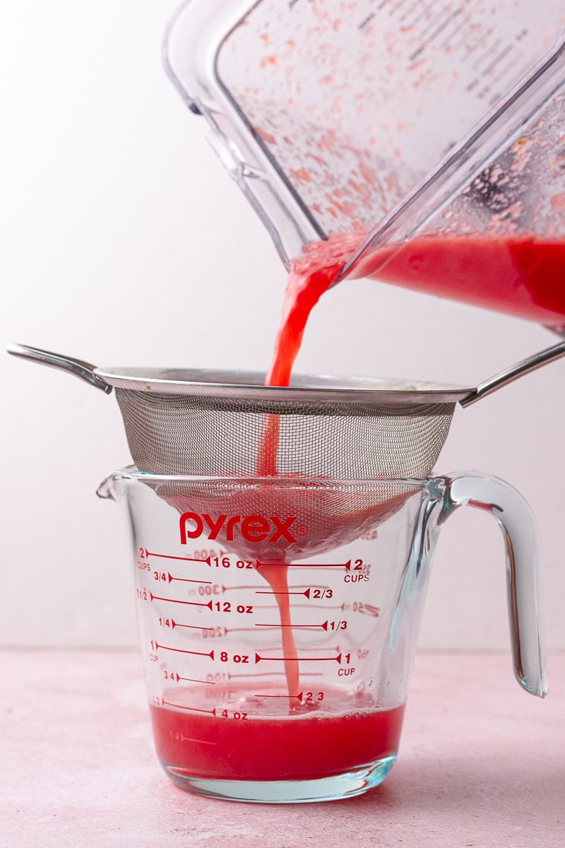 Blended watermelon juice being strained through a fine mesh sieve into a Pyrex measuring cup.