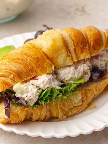 Waldorf chicken salad croissant sandwich plated with fresh greens and apple slices, styled for a blog hero image.