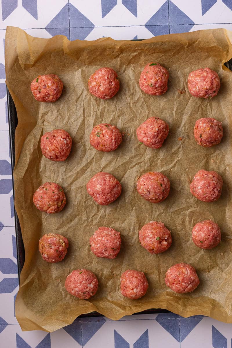 Uncooked lamb meatballs are portioned and arranged on a parchment-lined baking sheet.