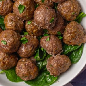 Overhead view of juicy cooked lamb meatballs garnished with parsley on a bed of spinach.