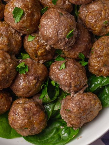Overhead view of juicy cooked lamb meatballs garnished with parsley on a bed of spinach.