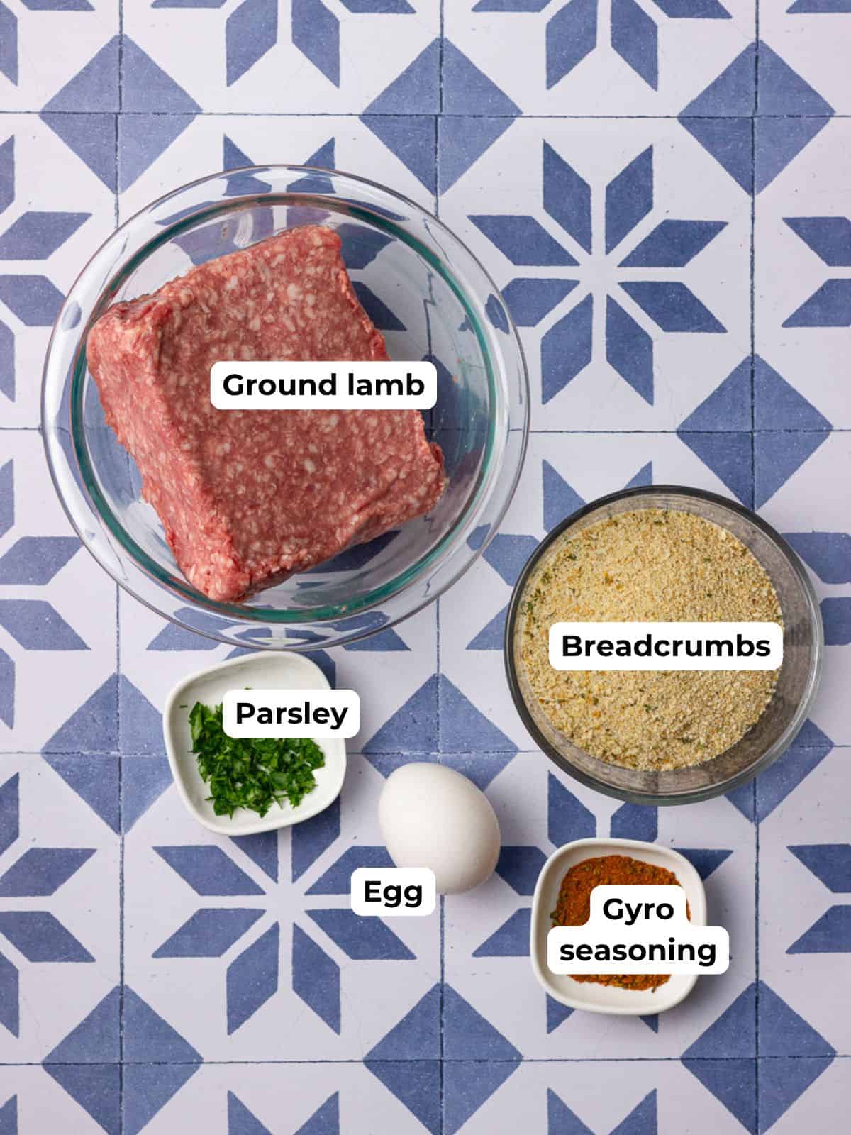 Labeled ingredients including ground lamb, parsley, egg, breadcrumbs, and gyro seasoning are arranged on a patterned tile surface.