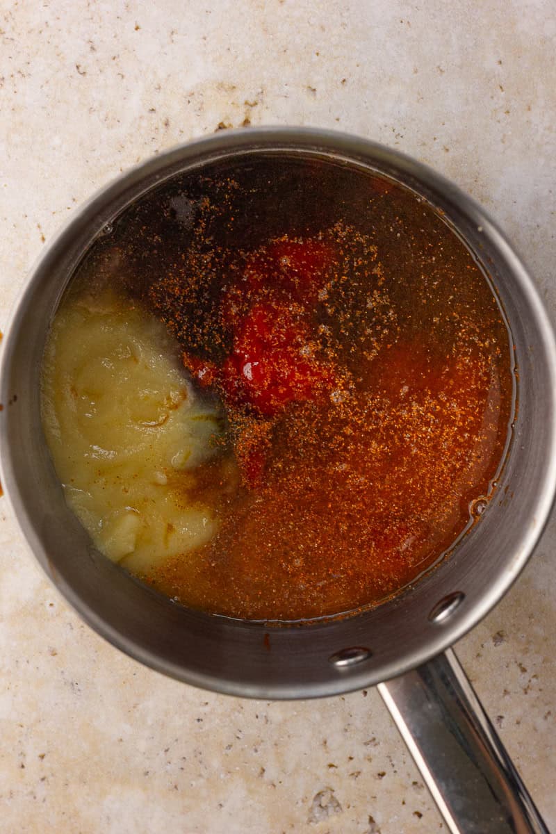 A saucepan with bbq ingredients including ketchup, applesauce, and spices before mixing.