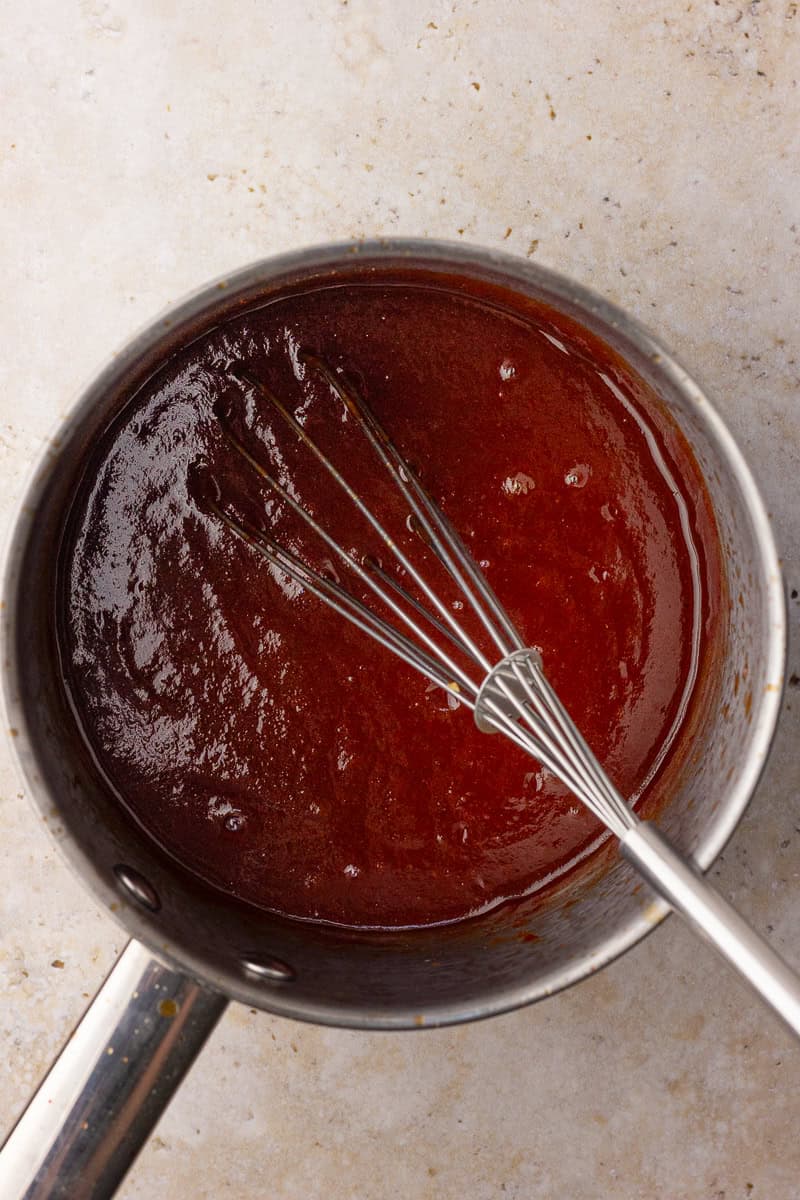 Apple BBQ sauce simmering on the stovetop in a saucepan.