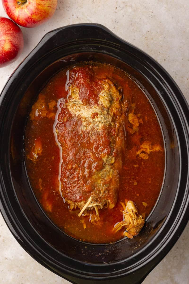 Fork-tender pork being shredded directly in the slow cooker after cooking.