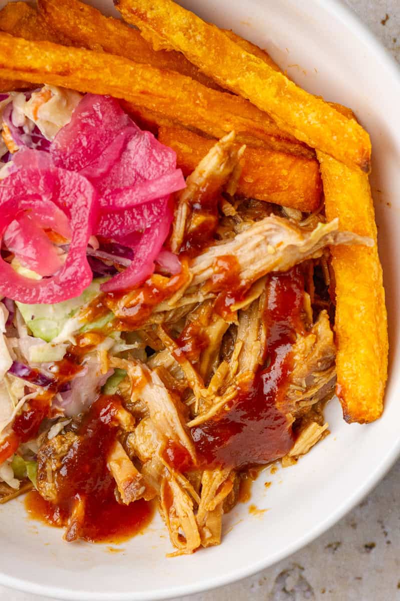 Pulled pork BBQ bowl with sweet potato fries, slaw, and pickled onions.