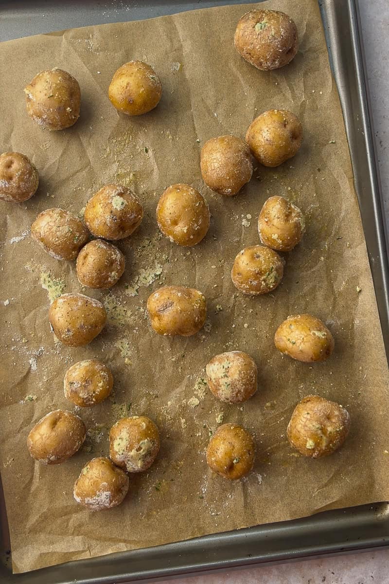 Golden petite potatoes tossed in ranch seasoning are spread across a parchment-lined baking sheet, ready for roasting.