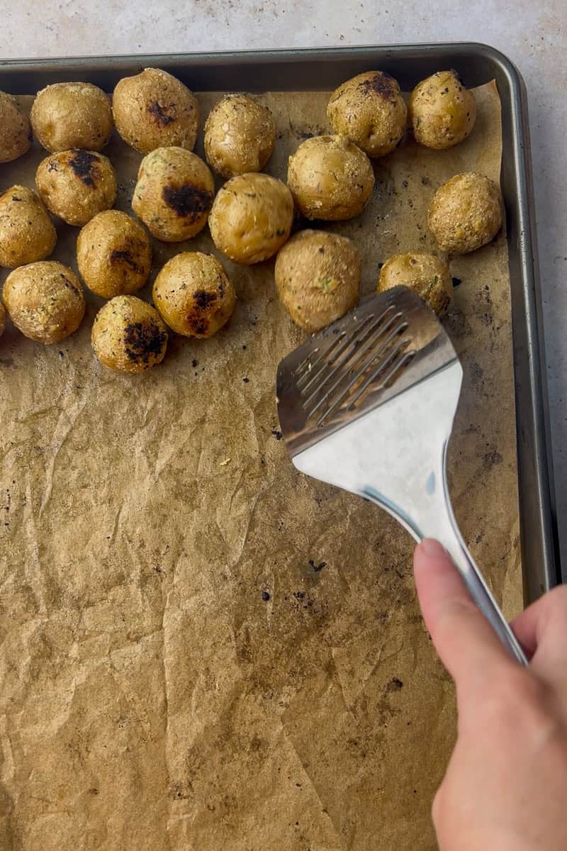 A metal spatula pushes the roasted potatoes to the side of the pan to make room for adding the chicken and broccoli.