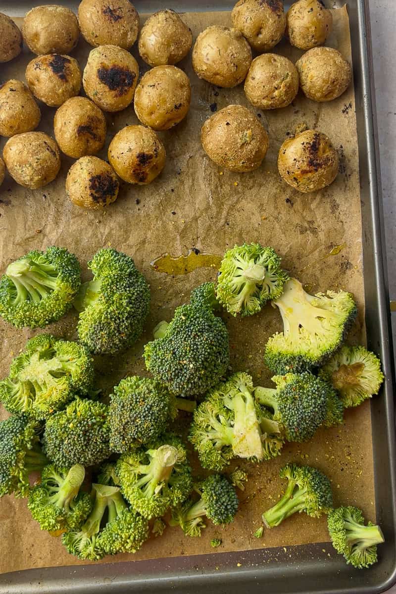 Fresh broccoli florets are added to one side of the sheet pan alongside already-roasted golden potatoes.