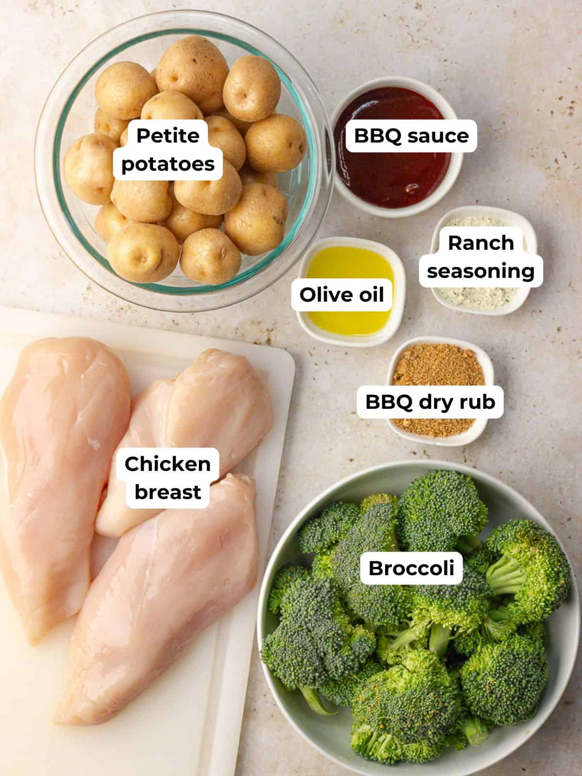 Labeled ingredients for BBQ sheet pan chicken, including chicken breast, petite potatoes, broccoli, olive oil, ranch seasoning, BBQ dry rub, and BBQ sauce.