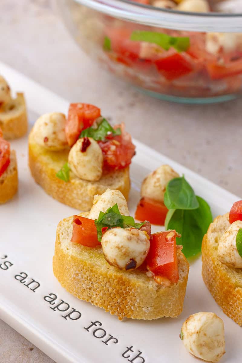 Close-up of spicy bruschetta caprese on toasted bread, topped with tomato, mozzarella, basil, and red pepper flakes.