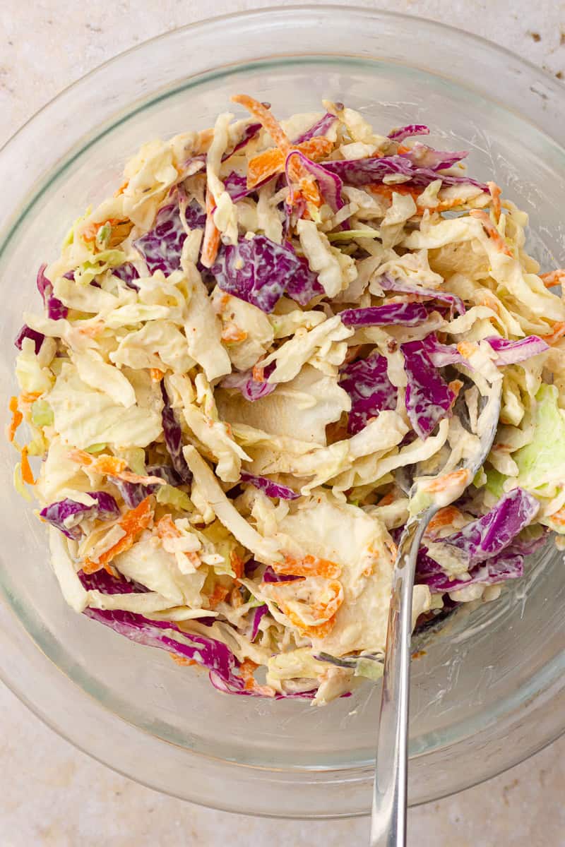 The creamy Cajun coleslaw fully mixed in a glass bowl with a spoon.
