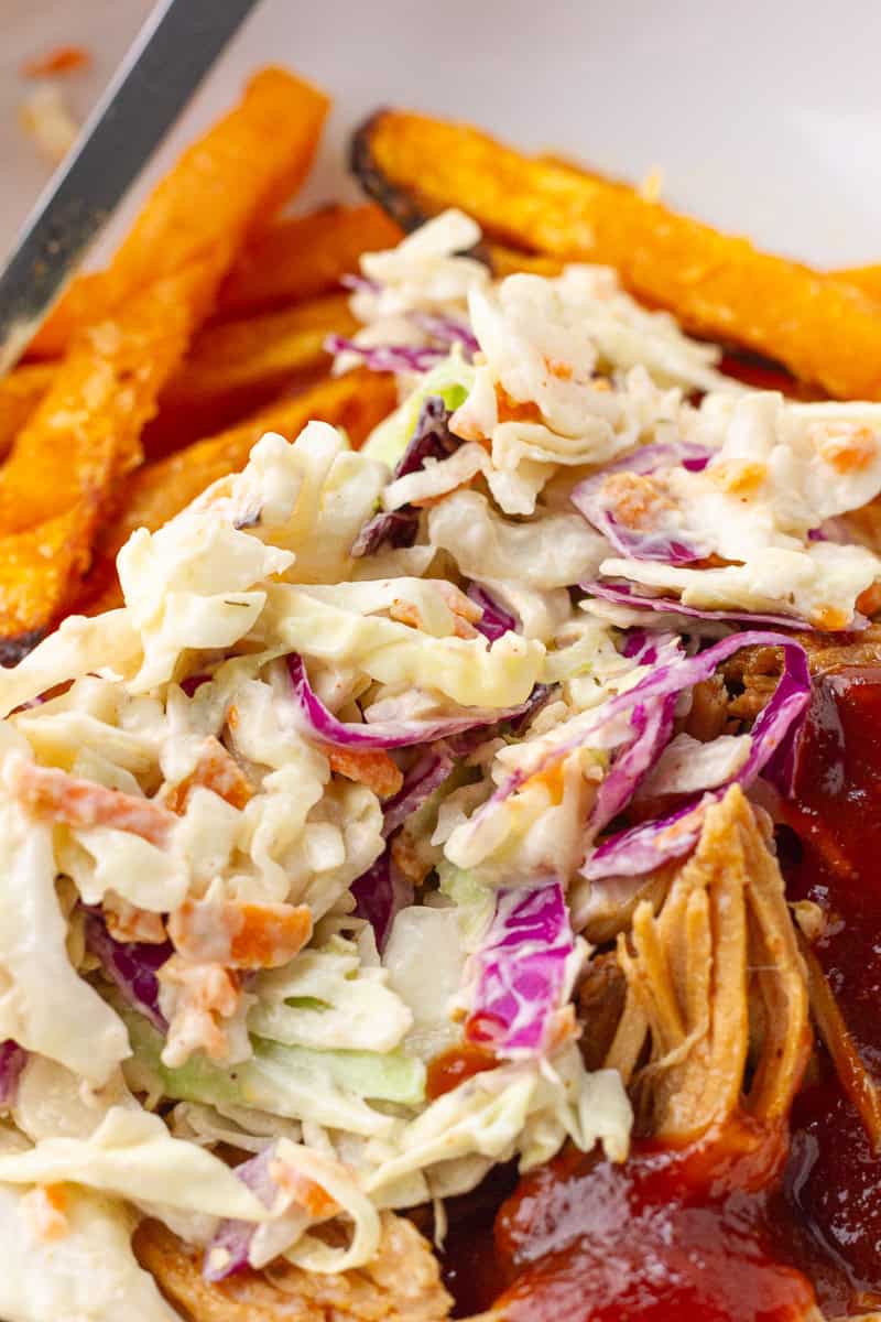 Cajun coleslaw served on a plate with pulled pork and sweet potato fries.