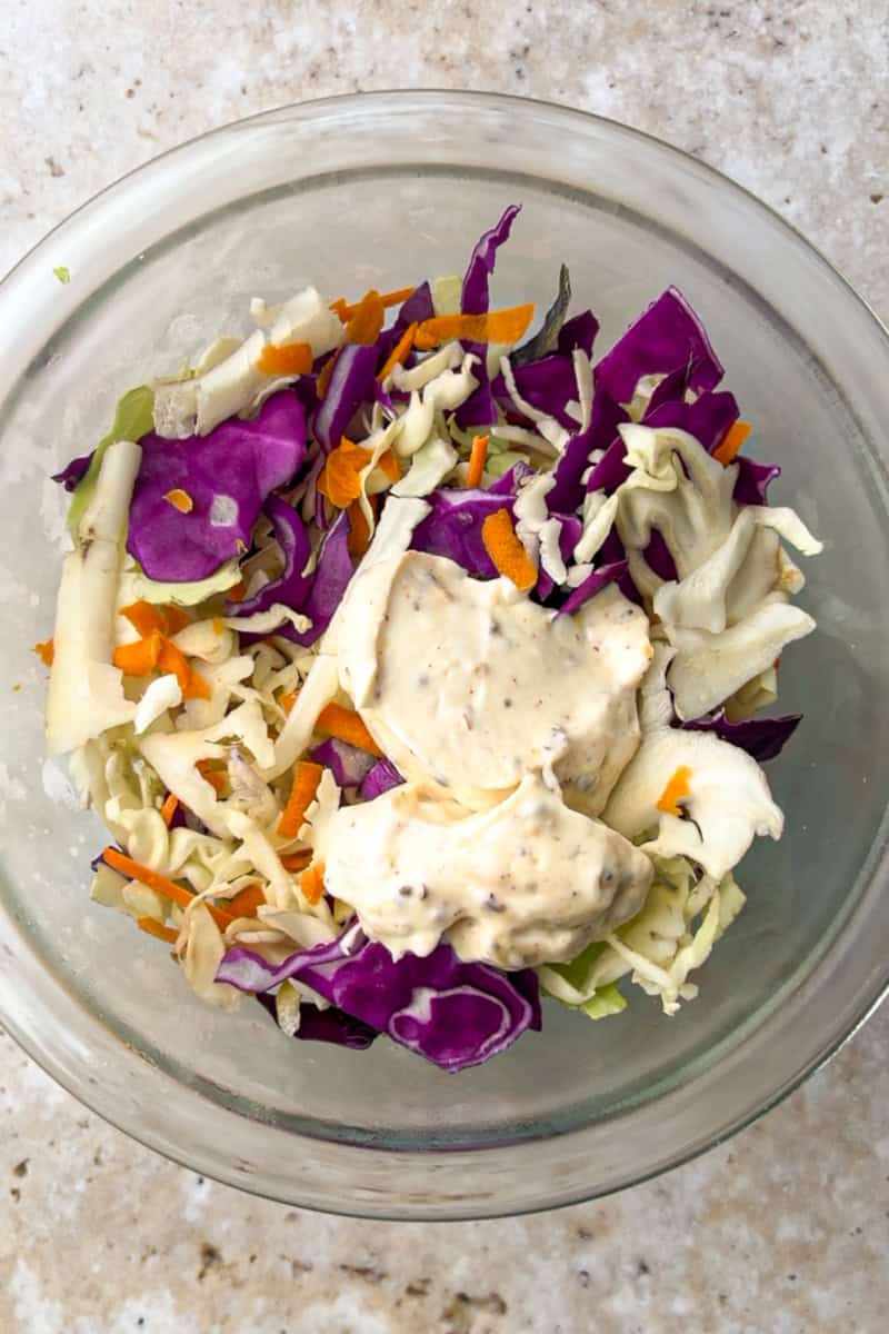 A bowl of tri-color slaw mix topped with creamy Cajun dressing before mixing.