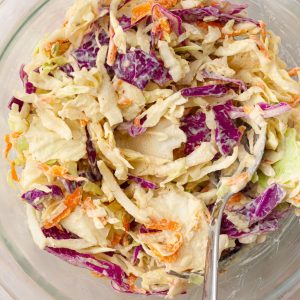 Close-up of creamy Cajun coleslaw in a glass bowl, showing colorful shredded cabbage and carrots.