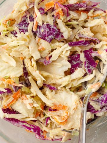 Close-up of creamy Cajun coleslaw in a glass bowl, showing colorful shredded cabbage and carrots.