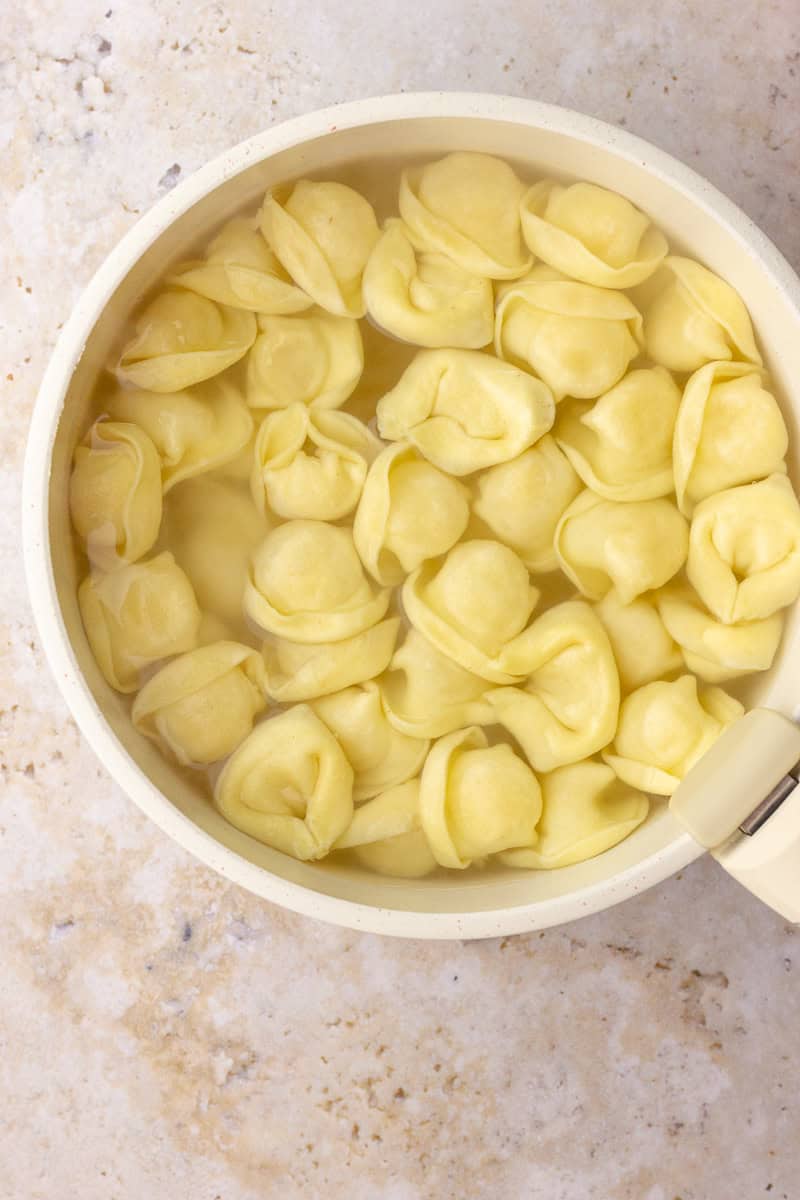 Cheese tortellini boil in a pot of water on the stovetop during prep for the Caprese skewers.