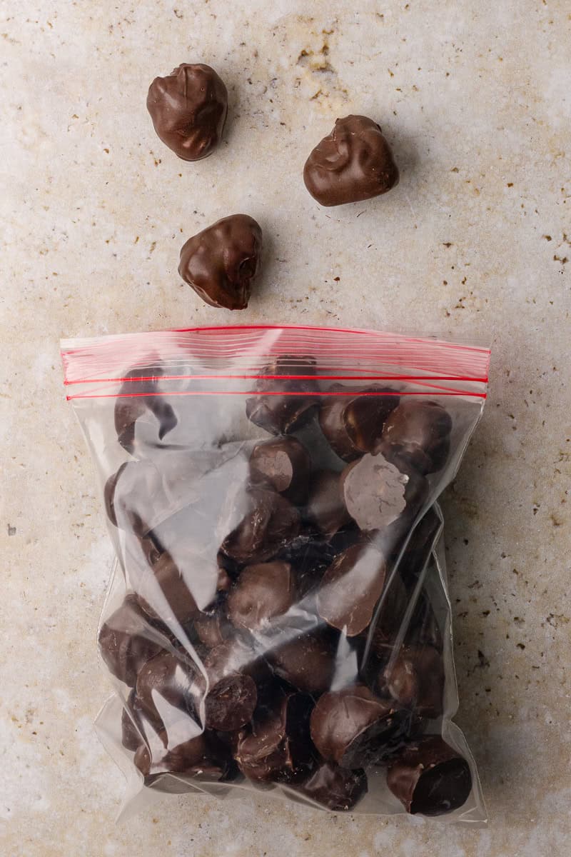 Finished chocolate covered raspberries stored in a plastic freezer bag with a few scattered on a countertop.