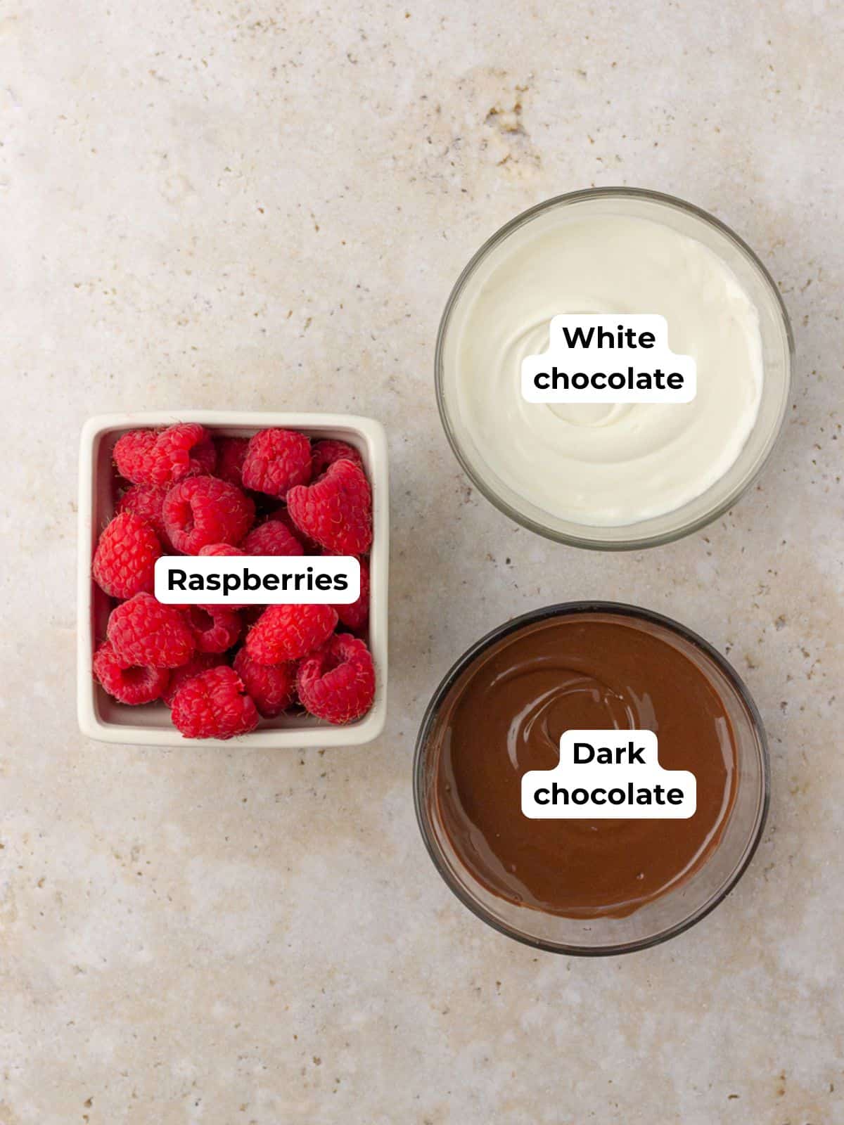 Three bowls showing the ingredients for the recipe: fresh raspberries, melted white chocolate, and melted dark chocolate.
