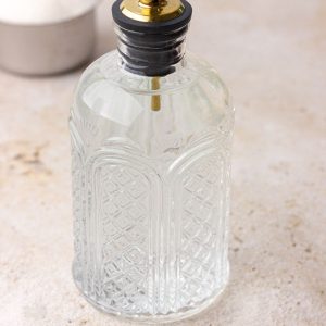 A close-up of a full syrup bottle filled with clear monk fruit syrup on a neutral background.
