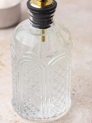 A close-up of a full syrup bottle filled with clear monk fruit syrup on a neutral background.