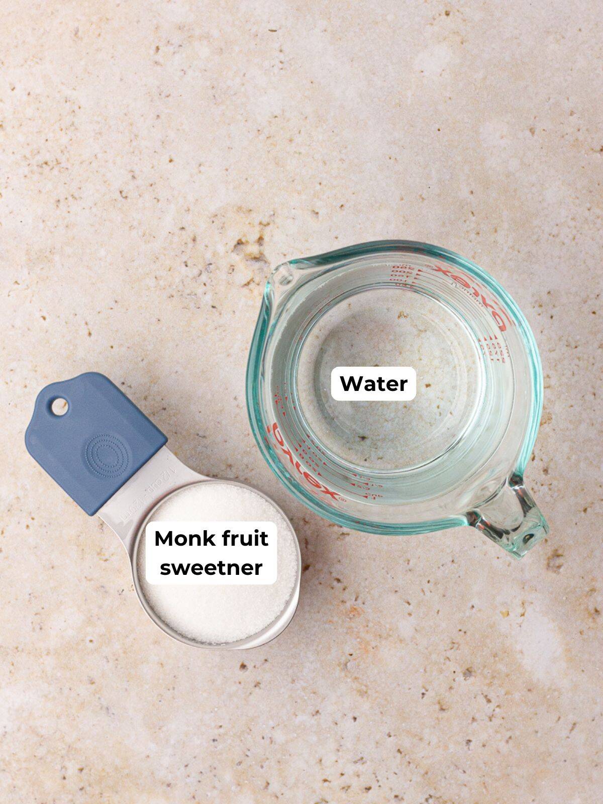 A measuring cup of monk fruit sweetener and a glass measuring cup of water labeled for ingredients.