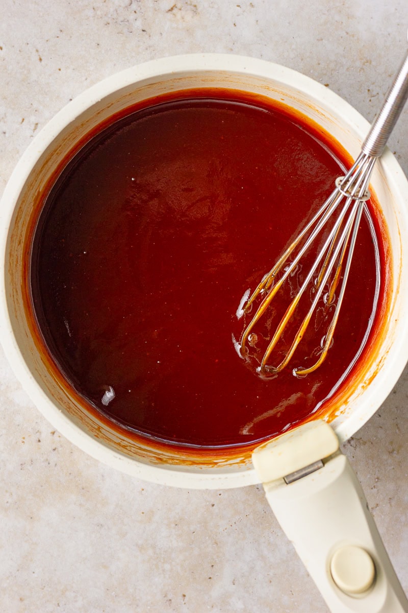 A saucepan with whisked peach BBQ sauce simmering gently on the stovetop.
