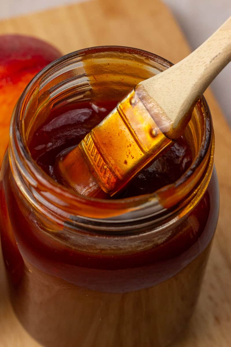 A close-up of thick peach BBQ sauce clinging to a wooden brush