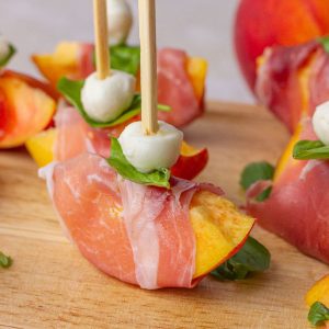 A close-up of a peach prosciutto skewer showing the layered mozzarella, basil, and peach.