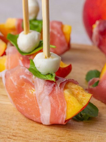 A close-up of a peach prosciutto skewer showing the layered mozzarella, basil, and peach.