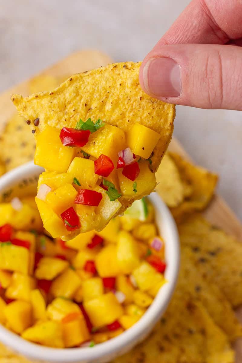 A close-up of pineapple mango habanero salsa scooped onto a tortilla chip for the perfect bite.