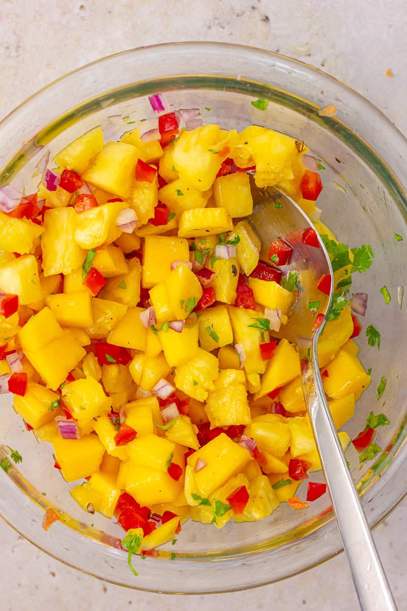 Freshly mixed pineapple mango habanero salsa in a glass bowl with a spoon.