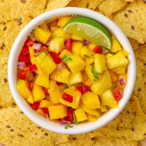 Top-down shot of vibrant pineapple mango habanero salsa in a bowl with lime and tortilla chips.