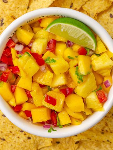 Top-down shot of vibrant pineapple mango habanero salsa in a bowl with lime and tortilla chips.
