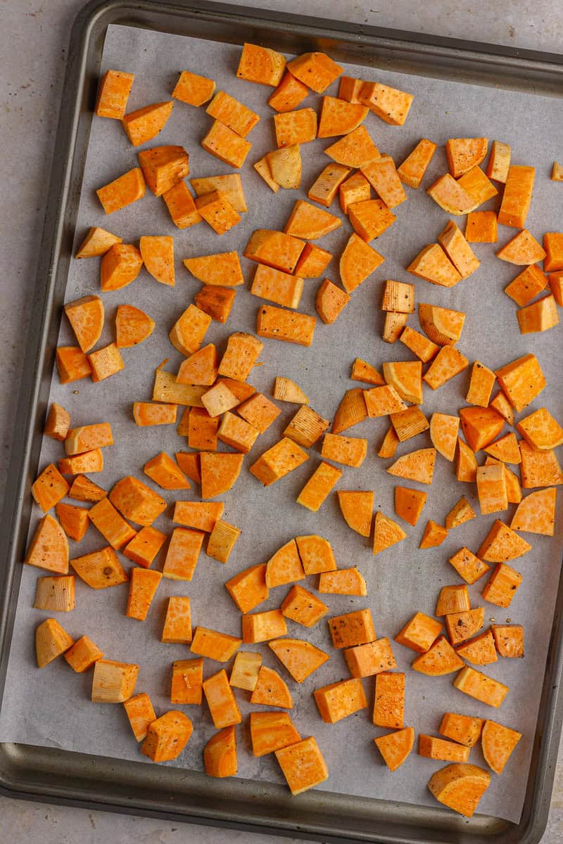 Cubed sweet potatoes spread out on a parchment-lined sheet pan for roasting.